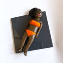 Figure of a black woman in an orange bikini, laying on a dark gray tile and sunbathing.