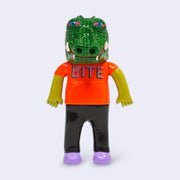 Vinyl figure of a man wearing an orange shirt that reads "bite" with a large crocodile head atop his head, with red glazed over eyes.