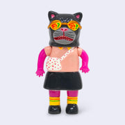 Vinyl figure of a pink woman, wearing a collared short sleeve shirt, a skirt and a crossbody bag. Atop her head is a large black cat mask with flashy looking sunglasses.