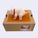 White vinyl figure of a cat, with large blue eyes, an open mouth and textured fur. It stands atop of a cardboard box.
