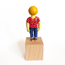 Figurine with a lemon head, wearing a red polka dot shirt and blue jeans on a wooden block with a white background