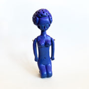 All purple sculpture of a nude woman sitting on her knees, with her arms at her side and a short perm-like hairstyle. 