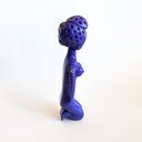 All purple sculpture of a nude woman sitting on her knees, with her arms at her side and a short perm-like hairstyle. 