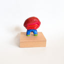 Colorful figurine with a red ribbed circular shape for its body and tiny legs, on a wooden block against a white background
