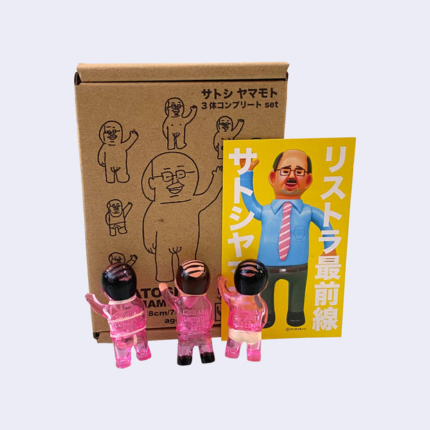 Set of 3 small vinyl figures of little business men. One wears a pink suit and waves. Another has black hair, pink skin and wears a tan briefs. The final figure has black hair, pink skin and wears pink bondage type attire. Back view.