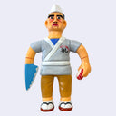 Vinyl figure of a dressed like a sushi chef, with a short gray kimono shirt with a logo for "All About Sushi". He hold a piece of sushi in one hand and his other hand is a knife.