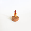 Tiny nude figurine of a woman with long reddish-brown hair and bangs. She stands on a circular wooden base.