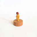 Tiny nude figurine of a woman with long reddish-brown hair and bangs. She stands on a circular wooden base.