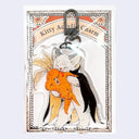 A packaged acrylic charm featuring an illustration of a white cat wearing a black cape and biting into an orange root vegetable, with a black clasp at the top and printed backing card reading 'Kitty Acrylic Charm'.