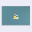 A rectangular teal envelope with a small central illustration of a yellow dinosaur hugging a white gift box with a blue bow, set against a light gray background.