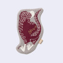 Die cut fabric coaster, shaped to the design of a burgundy raptor-like dinosaur perched on its hindlegs with small arms. Border is beige. Backside of coaster, which is also the back view of the design.