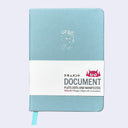 A light blue hardcover notebook with a white paper band around the middle. The band has the brand name 'DOCUMENT' and a small pink devil logo, along with the text 'PLOTS DOTS AND MANIFESTOS'.