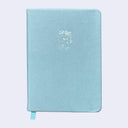 A light blue hardcover notebook with a small white embossed cartoon cat character on the front cover and a matching light blue ribbon bookmark hanging from the bottom edge, shown against a plain light gray background.