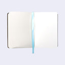 Open book spread showing the inner pages of the sketchbook, blank cream colored paper with a light blue ribbon which functions as a bookmark.