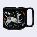 Black mug with a white dog and floral design on a light gray background