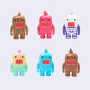 Six Domo-style character figurines arranged in two rows on a light gray background. The figures have different colorways: brown wood grain, pink, white with purple skeleton details, pastel yellow-to-green gradient, bright blue, and brown.
