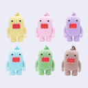 Six flocked Domo character toys arranged in two rows on a light gray background, shown in yellow, pink, purple, light blue, green, and beige.