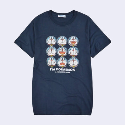 Dark navy blue t-shirt featuring graphics of Doraemon, making 9 different faces. Below reads "I'm Doraemon! A Hundred Faces"