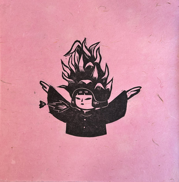 Black ink relief print on pink fibrous paper of a small girl with a dragonfruit atop of her head. Her arms are extended out and small flames appear around her mouth.