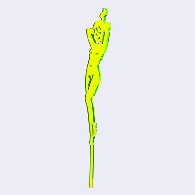 Neon green die cut drink stirrer of a nude cartoon girl, standing with her hands behind her head and wearing her hair in a ponytail.