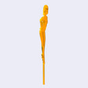 Orange die cut drink stirrer of a nude cartoon girl, standing with her hands behind her back and with a short bob haircut. Side view.