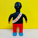 Toy figure with a black head, red body, and blue shoes against a yellow background