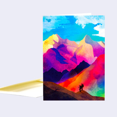 Greeting card with a brightly colored illustration of 2 silhouetted hikers standing small on very large mountains.