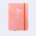 Peach colored pleather covered sketchbook with a small embossment of a robot carrying a flag that reads "Giant Robot" in the upper center. A bright orange elastic band keeps the sketchbook closed.