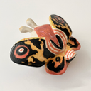 Ceramic sculpture of a small character with a large head wearing a Mothra costume, with a hood hat and a large set of wings behind it matching Mothra's colorways.