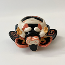 Ceramic sculpture of a small character with a large head wearing a Mothra costume, with a hood hat and a large set of wings behind it matching Mothra's colorways.
