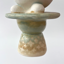 Ceramic sculpture of a platform, akin to the bottom of a candle holder, with a white bunny character popping out of the top.
