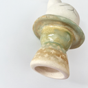 Ceramic sculpture of a platform, akin to the bottom of a candle holder, with a white bunny character popping out of the top.