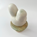 Ceramic sculpture of a platform, akin to the bottom of a candle holder, with a white bunny character popping out of the top.