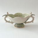 Ceramic vessel, a wide teacup with 2 handles. The bowl of the cup is shaped like a flower and the handles have thorns on them. Atop each handle is a small white bunny character.