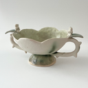 Ceramic vessel, a wide teacup with 2 handles. The bowl of the cup is shaped like a flower and the handles have thorns on them. Atop each handle is a small white bunny character.
