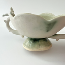 Ceramic vessel, a wide teacup with 2 handles. The bowl of the cup is shaped like a flower and the handles have thorns on them. Atop each handle is a small white bunny character.