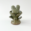 Small ceramic sculpture of a plant with leaves and a thorny base. Coming out the top is a bunny's head.