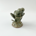 Small ceramic sculpture of a plant with leaves and a thorny base. Coming out the top is a bunny's head.