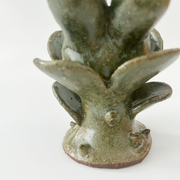 Small ceramic sculpture of a plant with leaves and a thorny base. Coming out the top is a bunny's head.