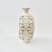 Cream colored ceramic vase with a very round body and a small fluted top, almost resembling a pomegranate in shape. On the side is a design of flowers.