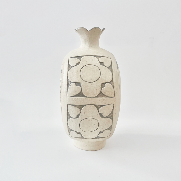 Cream colored ceramic vase with a very round body and a small fluted top, almost resembling a pomegranate in shape. On the side is a design of flowers.