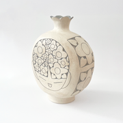  Cream colored ceramic vase with a very round body and a small fluted top, almost resembling a pomegranate in shape. On the front is a design of a person's head with floral patterned hair.