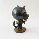 Dark brown ceramic sculpture of a character with a large head, large ears and a tiny body. They have horns and earring cuffs. They stand and hold a white flower with a thorny stem.