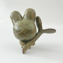 Small green ceramic figure of a bunny character with a large head and a tiny body. It holds a large plant sprout.