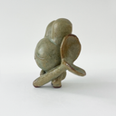 Small green ceramic figure of a bunny character with a large head and a tiny body. It holds a large plant sprout.
