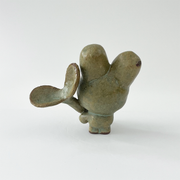 Small green ceramic figure of a bunny character with a large head and a tiny body. It holds a large plant sprout.