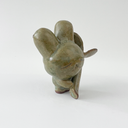 Small green ceramic figure of a bunny character with a large head and a tiny body. It holds a large plant sprout.