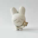Small white ceramic sculpture of a bunny character with a calm, closed eye expression. It has a large head and a tiny body, holding a star.
