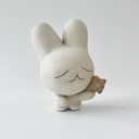 Small white ceramic sculpture of a bunny character with a calm, closed eye expression. It has a large head and a tiny body, holding a star.