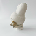 Small white ceramic sculpture of a bunny character with a calm, closed eye expression. It has a large head and a tiny body, holding a star.